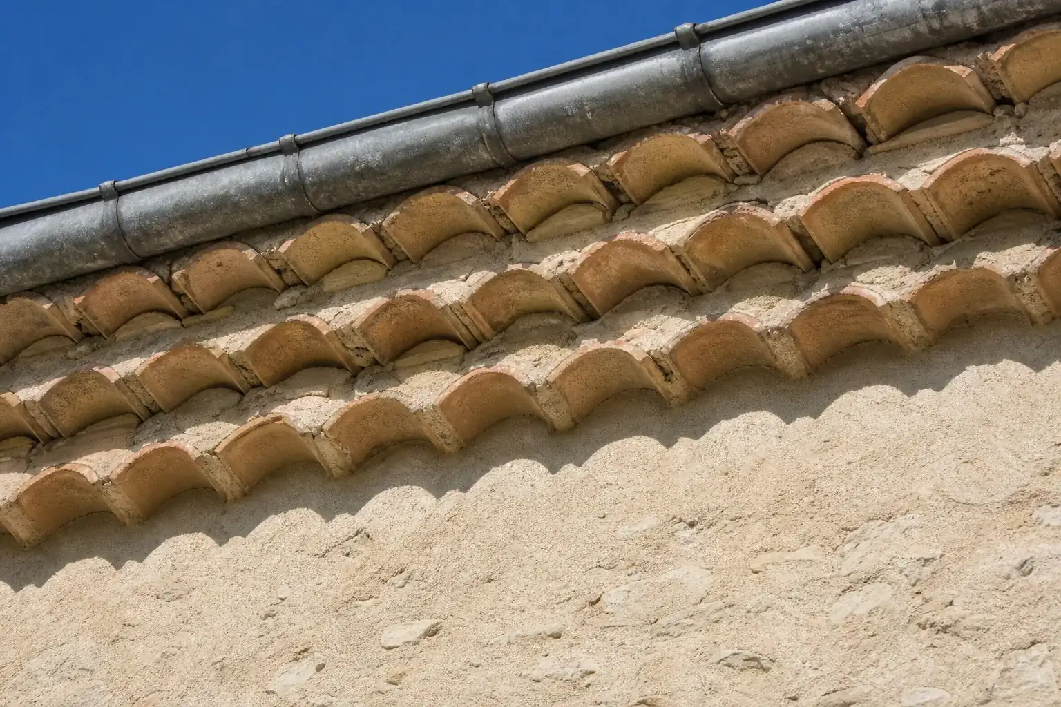 Génoise de trois rangs de tuiles en débord progressif sous l’avant-toit d’une maison enduite