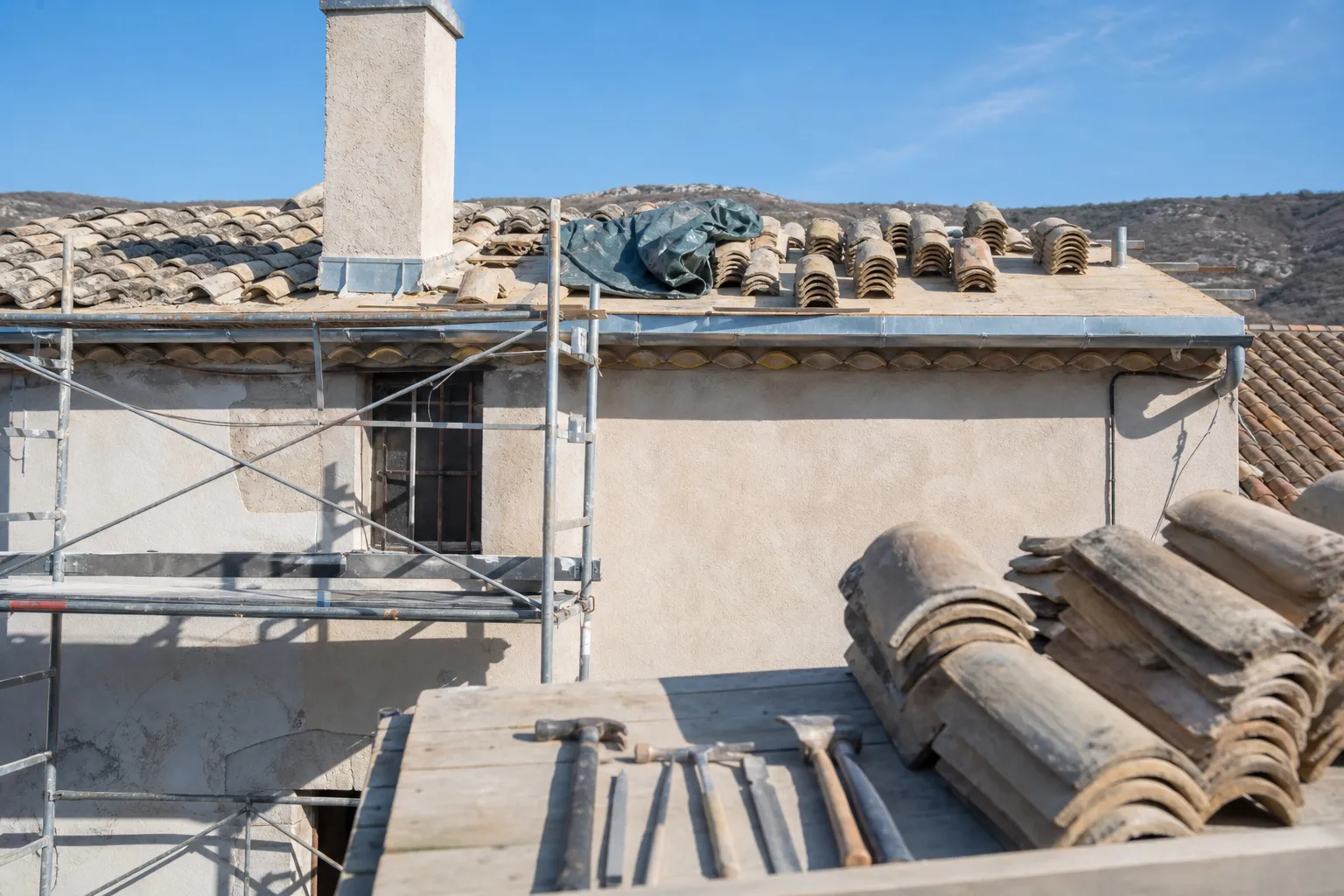 Échafaudage de chantier contre une façade enduite, tuiles canal triées en piles sur le voligeage