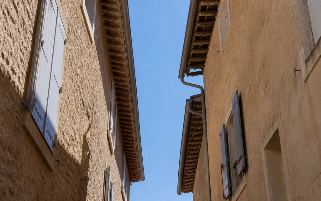 Ruelle ancienne vue vers le haut, bande de ciel serrée entre deux avant-toits de tuile