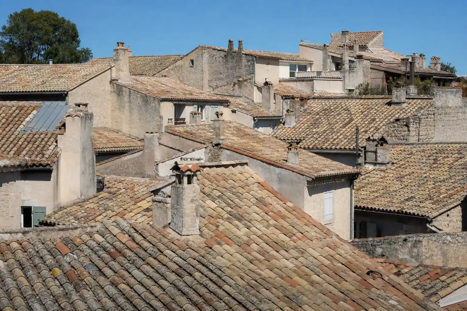 Toits du centre ancien vus d’en haut : nappe de tuiles blondies, souches enduites, faîtages parallèles